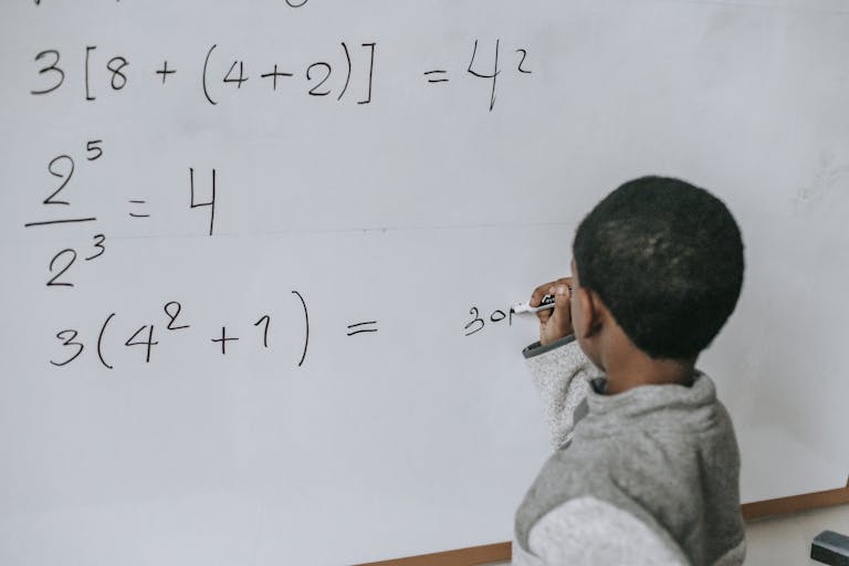 Focused child solving equations on a whiteboard, showcasing education and problem-solving skills.
